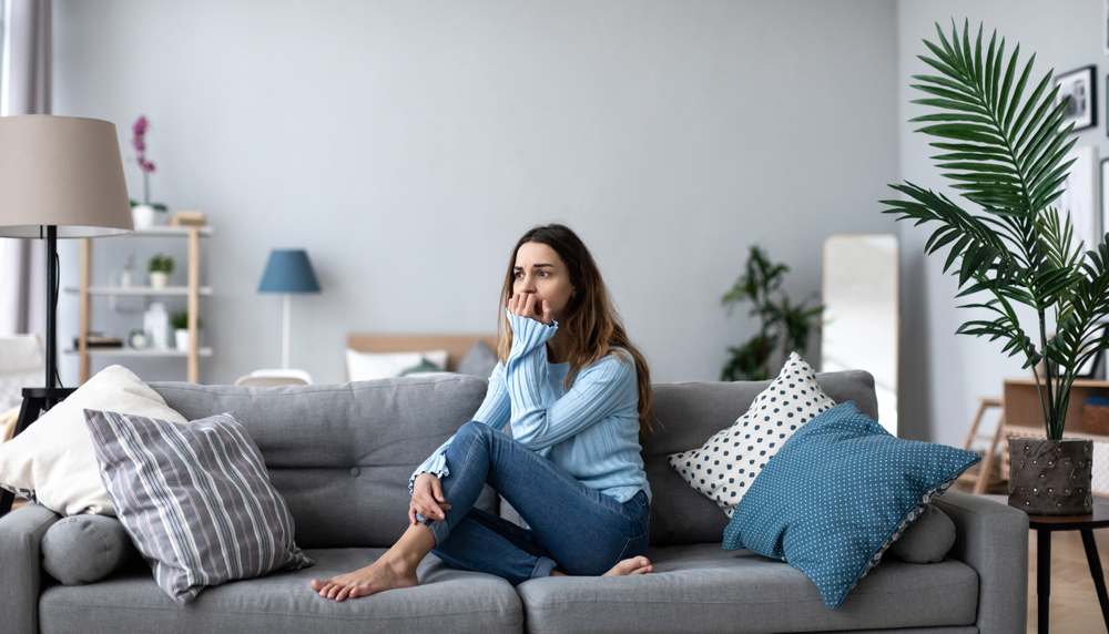 Upset young woman thinking about problem sitting alone on couch at home psychological problem 1